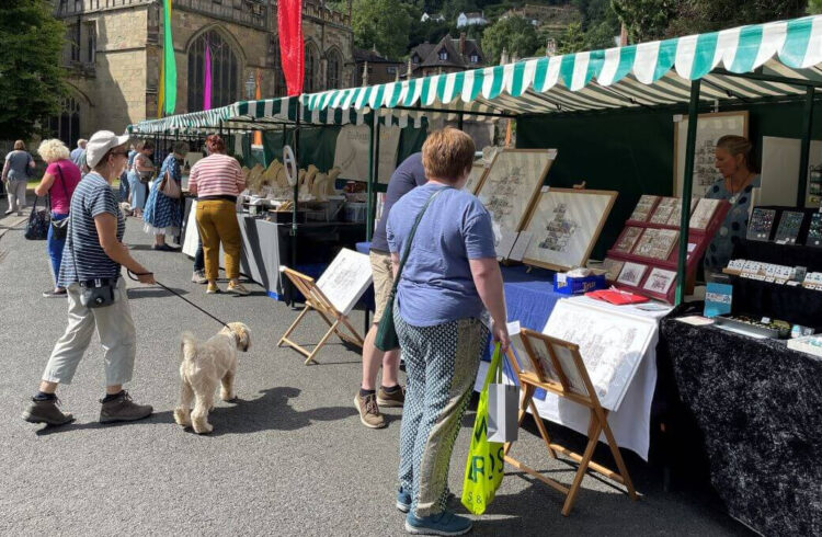 Stalls at the Malvern Arts Market and members of the public looking at the things for sale and a beige dog.