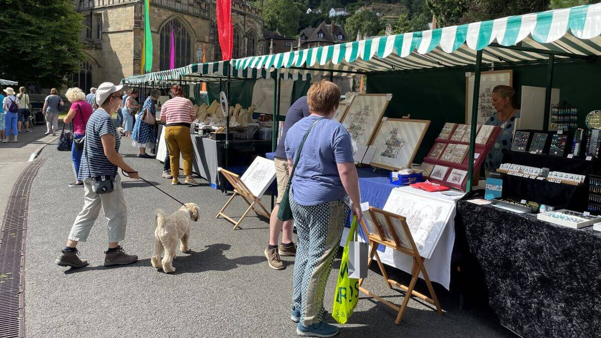 Stalls at the Malvern Arts Market and members of the public looking at the things for sale and a beige dog.