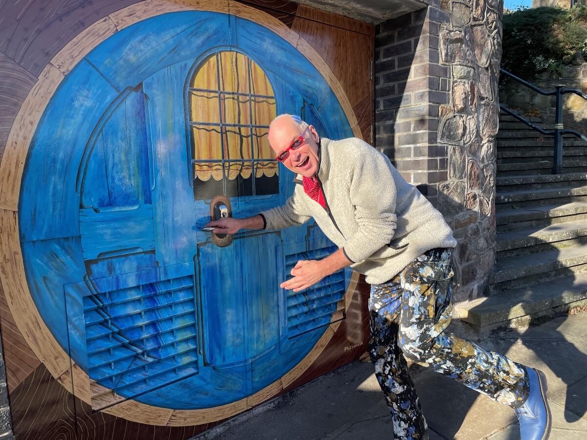Man poses with life size painting of blue Hobbit door