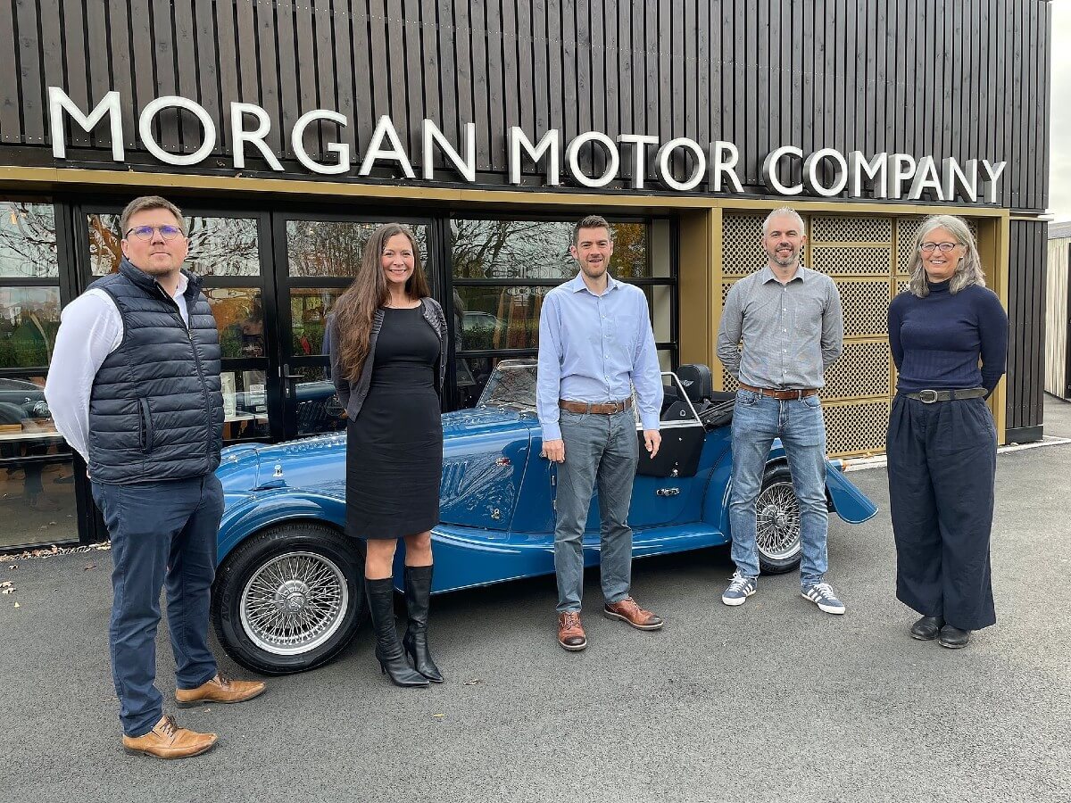 five people stand in front of a Morgan car
