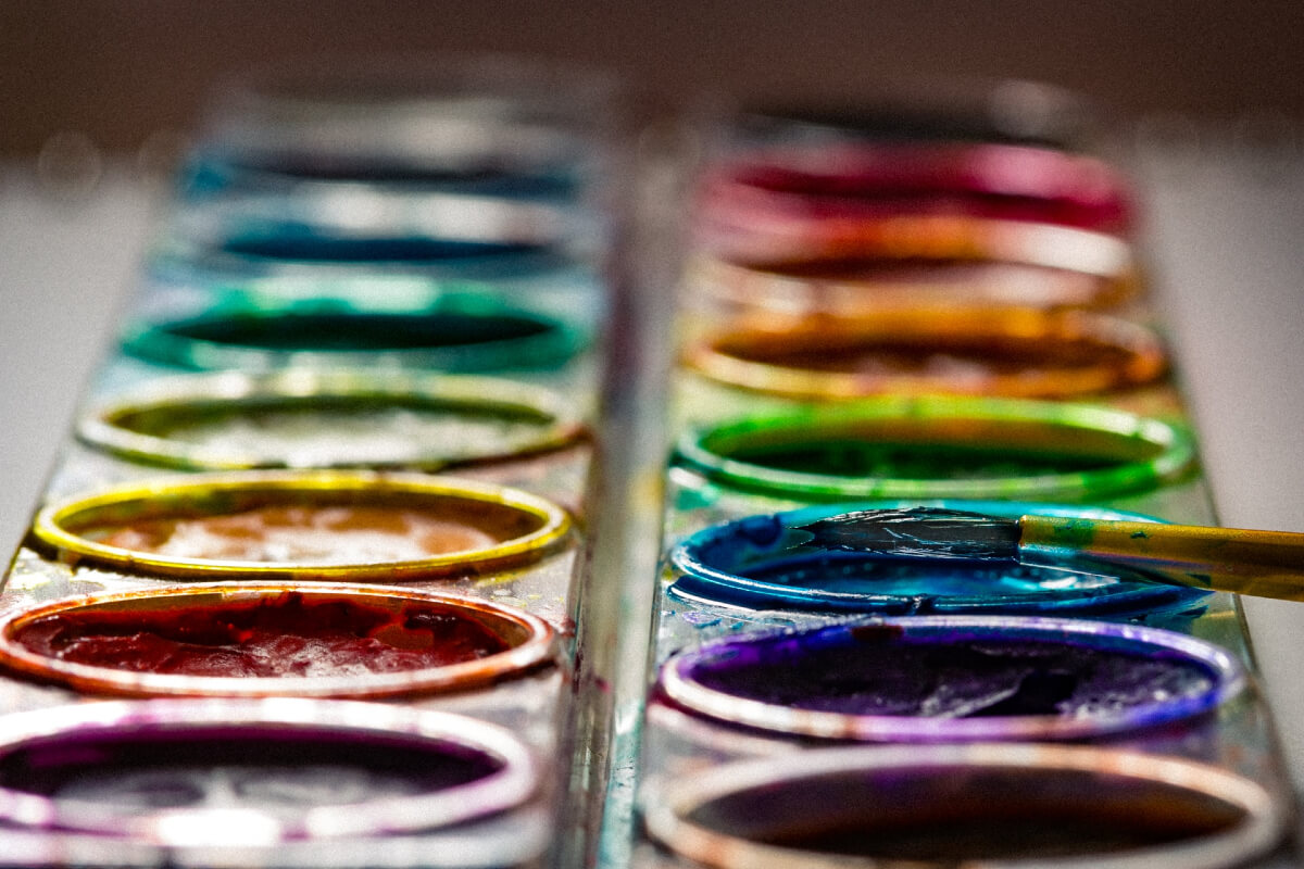 A close up of a colourful paint palette and a paint brush