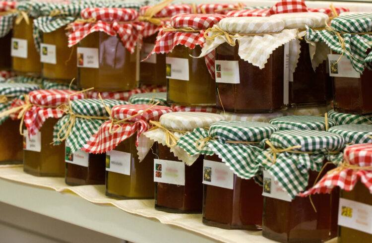 Jars full of jam and chutneys with material on the top.