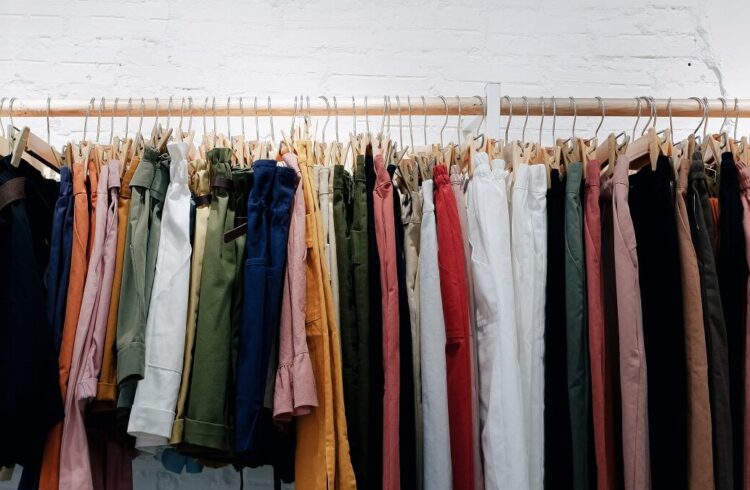A selection of trousers and shorts of various colours hanging on a rail with a white painted wall behind