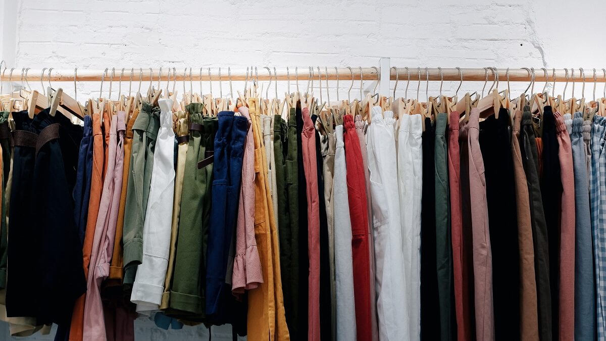 A selection of trousers and shorts of various colours hanging on a rail with a white painted wall behind