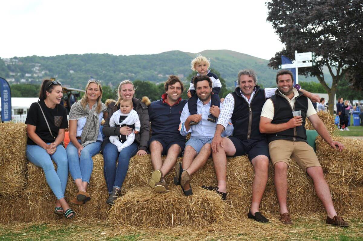 A group of friends and family smile sitting on hay bales