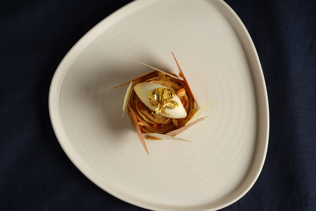A dish presented on an egg-shaped plate with gold leaf on top