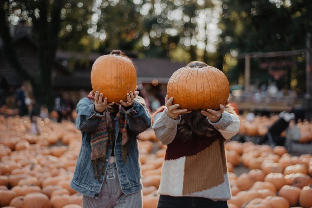 Two children holding pumpkins in front of their faces.