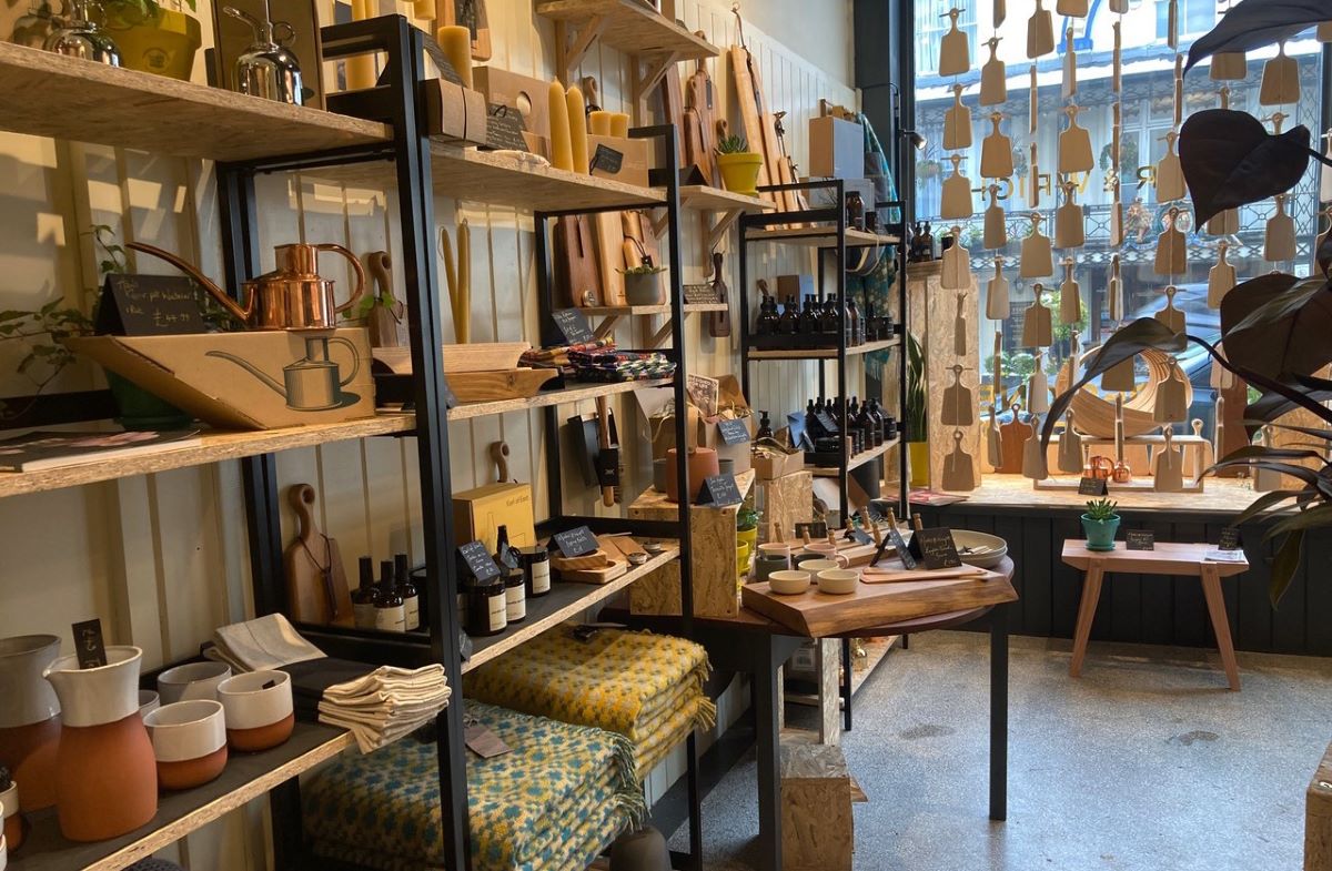Shop interior showing open wooden shelving with wool blankets, pottery, candles and kitchenware