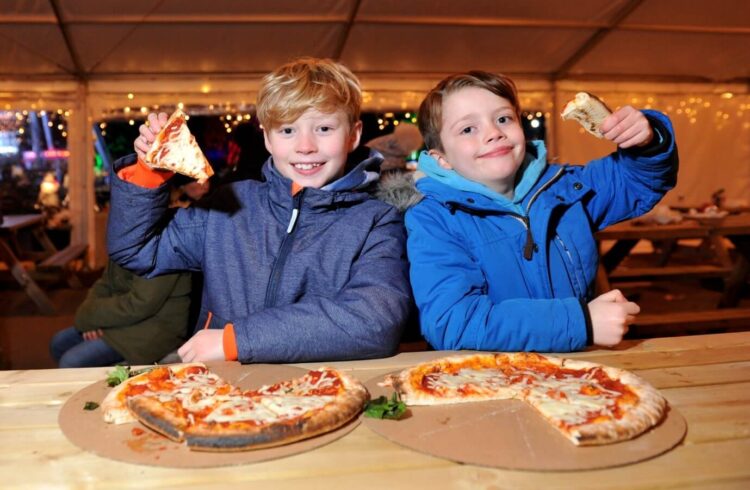 Two boys hold up pizza slices