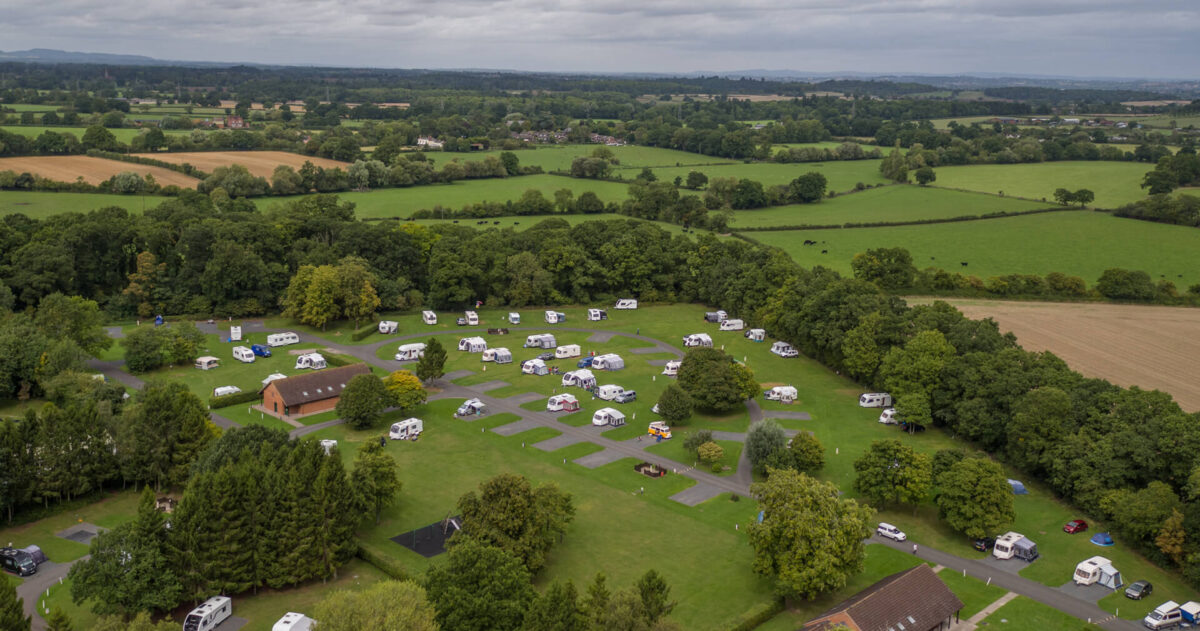 Aerial view of a caravan site with tree edged fields and white campervans in the park