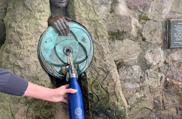 a water fountain shaped like a woman fills a reusable water bottle