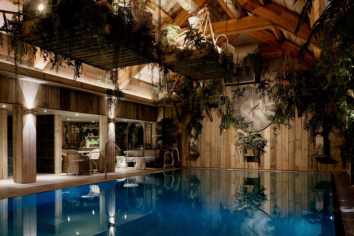 Indoor swimming pool with plants placed above and around reflected in the water