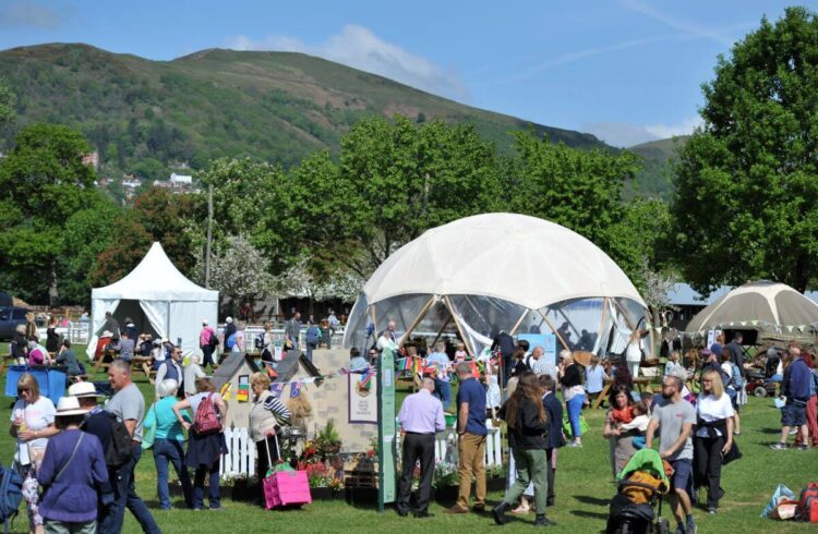 People looking at stalls at a festival with the Malvern Hills in the backdrop