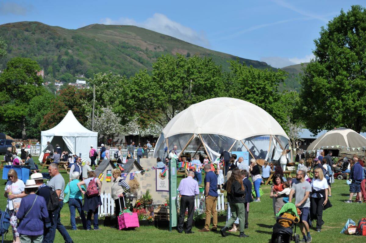 People looking at stalls at a festival with the Malvern Hills in the backdrop