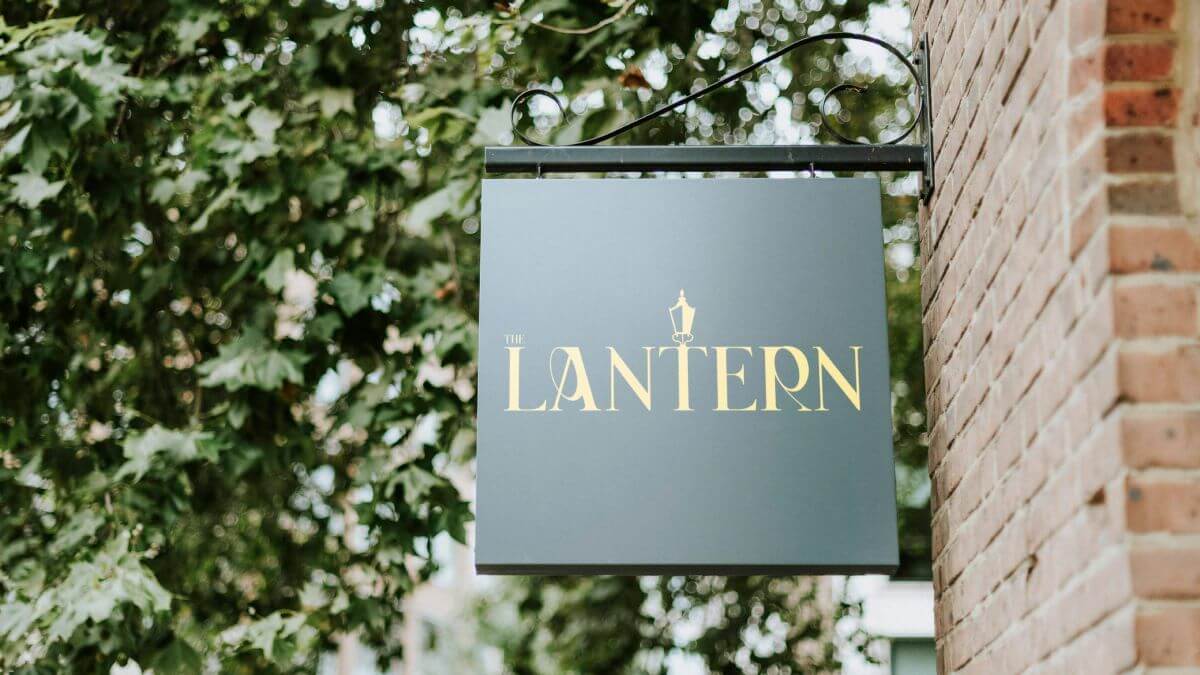 A forest green sign with swirling yellow writing which reads  "Lantern"