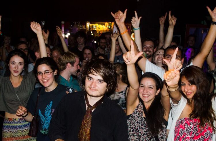 A crowd of young people raise their hands at a nighttime venue