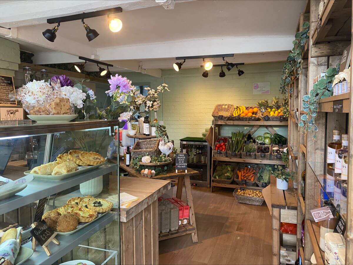 Small local produce deli with flowers, wooden shelving and sage green walls 