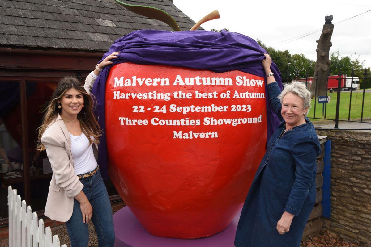 Two people unveiling a giant red apple