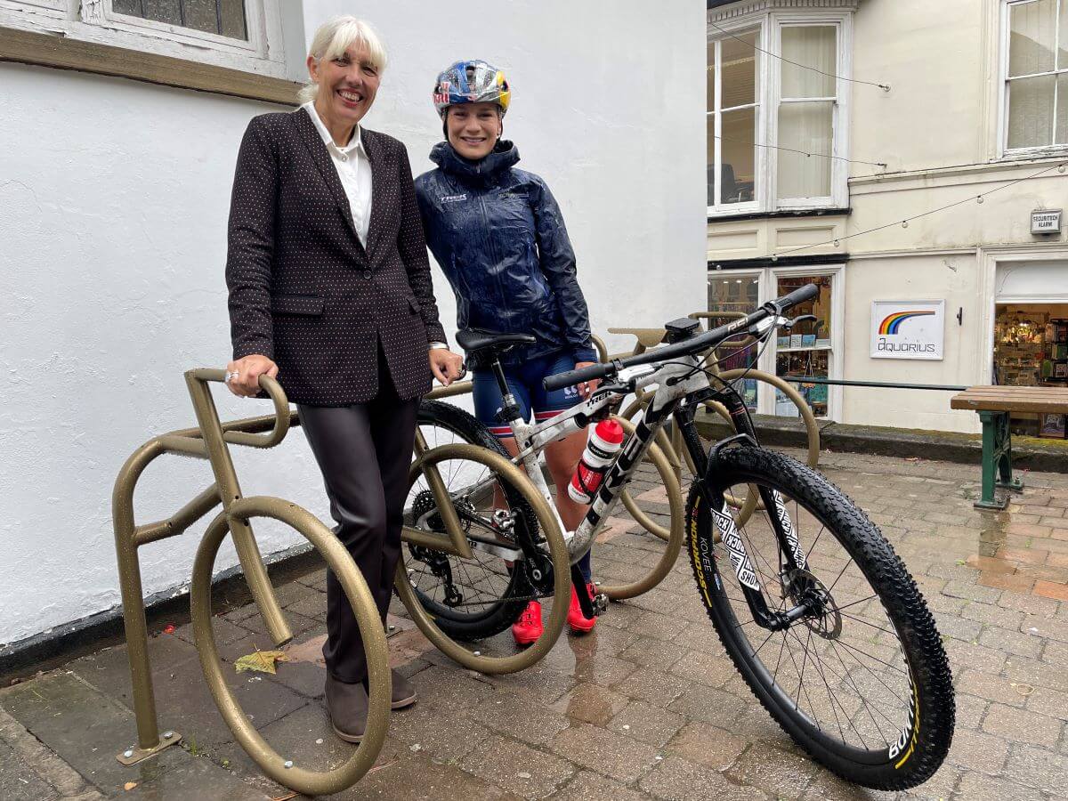 One cyclist and one person pose with golden painted bike racks shaped like bikes