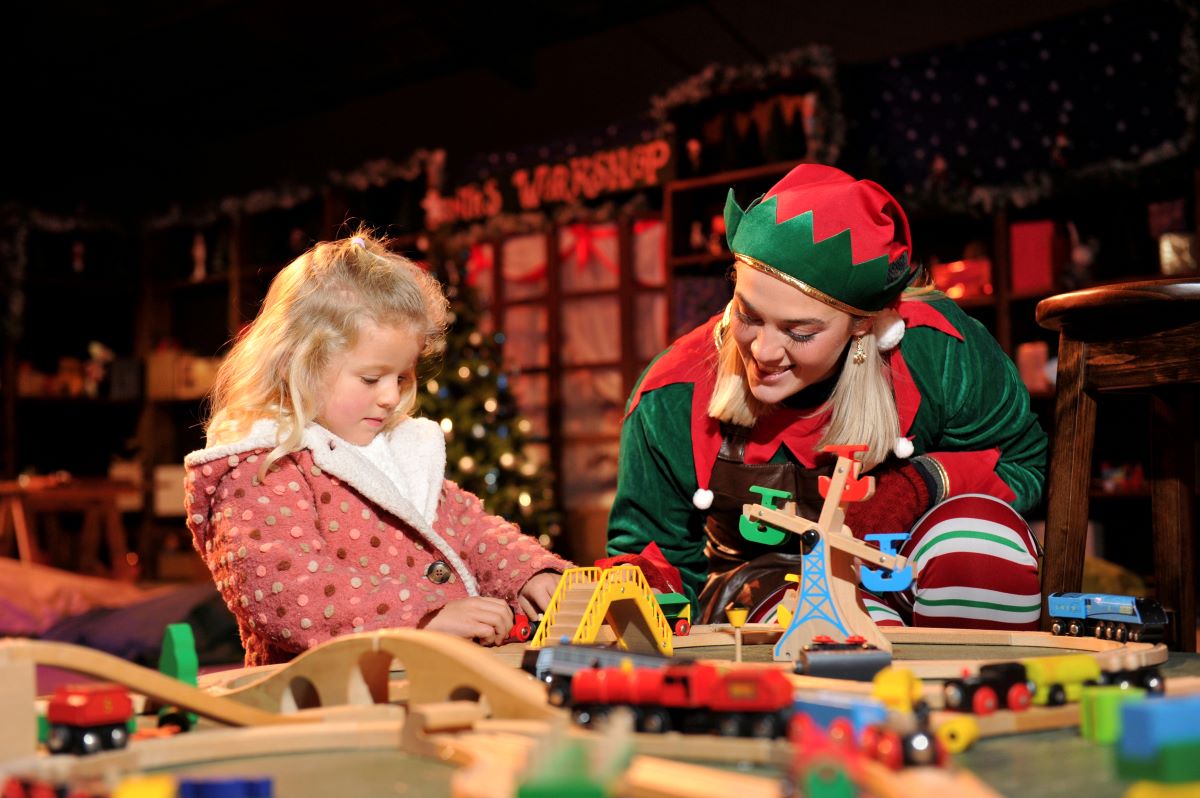 A Christmas elf plays with a child in a Christmas themed environment