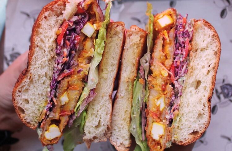 Two halves of a sandwich held so you can see cheese, coleslaw and lettuce inside
