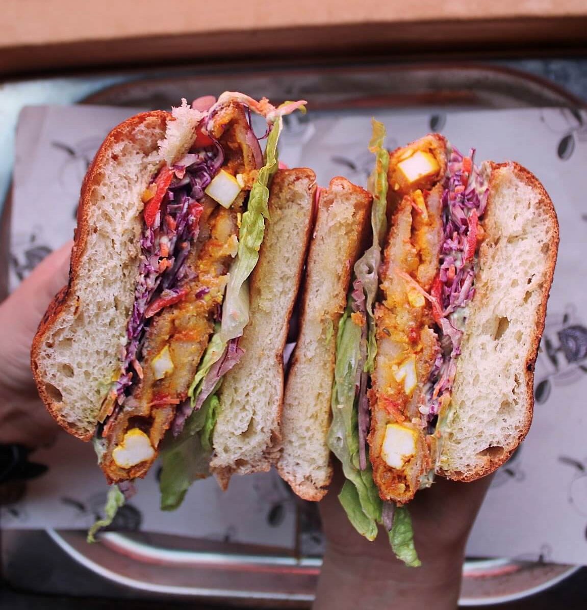 Two halves of a sandwich held so you can see cheese, coleslaw and lettuce inside