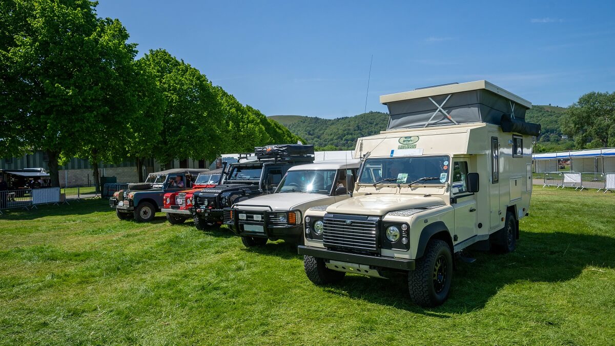 A variety of Land Rovers parked in a row with view of the Malvern Hills in the background