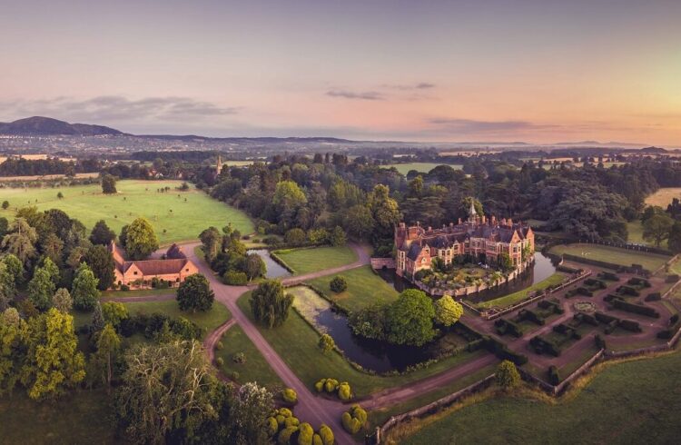 Aerial view of Madresfield Court with moat and gardens and outline of Malvern Hills in background