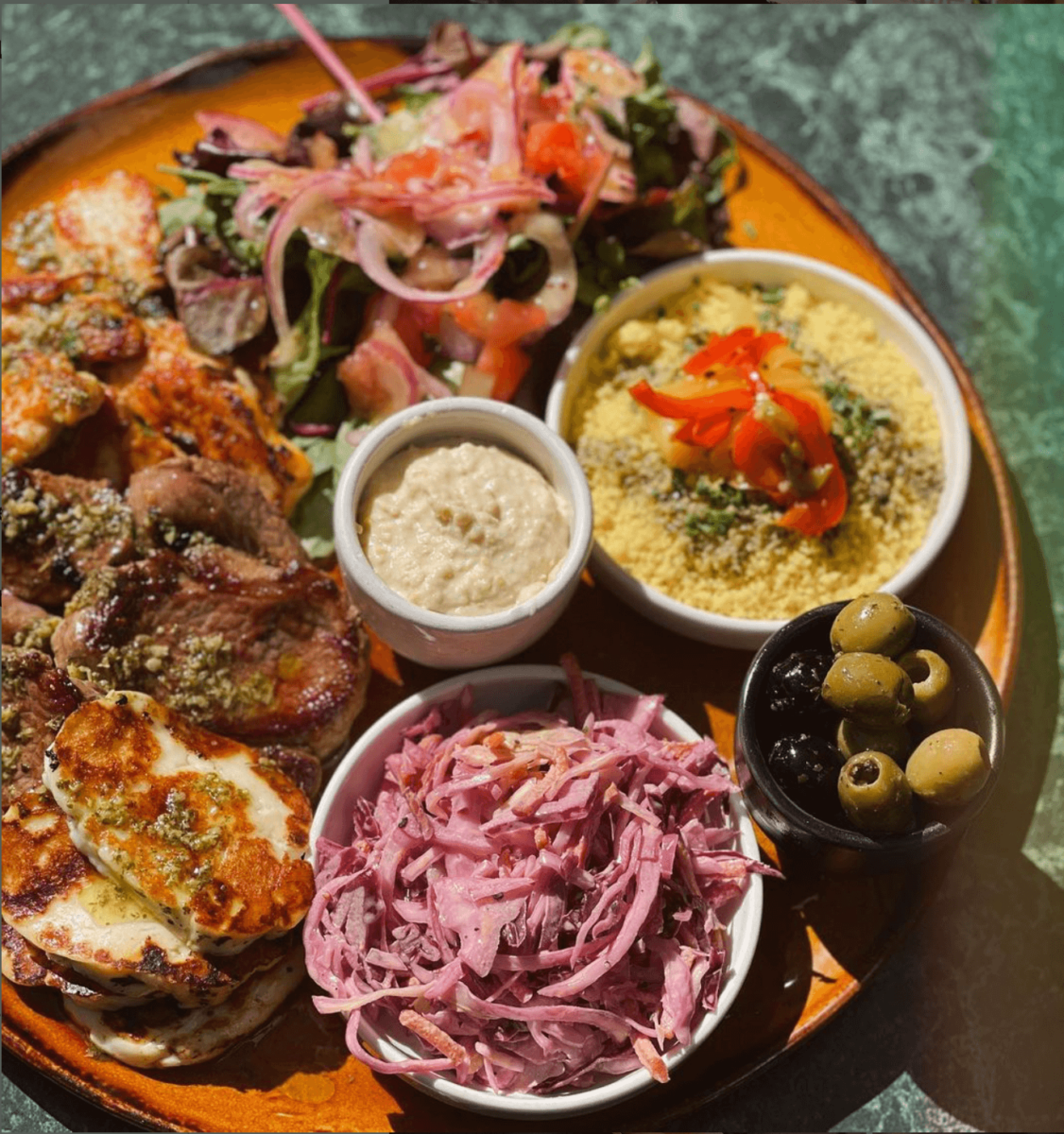 A meze plate with olives, salad, coleslaw, couscous, hummus and grilled halloumi