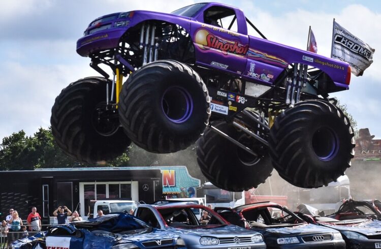 A monster truck leaping over several parked cars