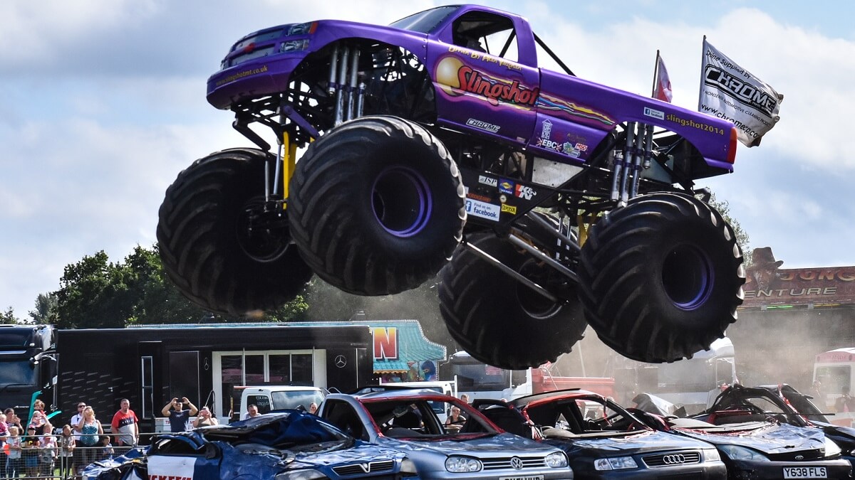 A monster truck leaping over several parked cars