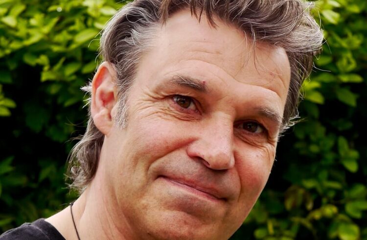 An image of Julian Hight looking straight at the camera, with leaves in the background