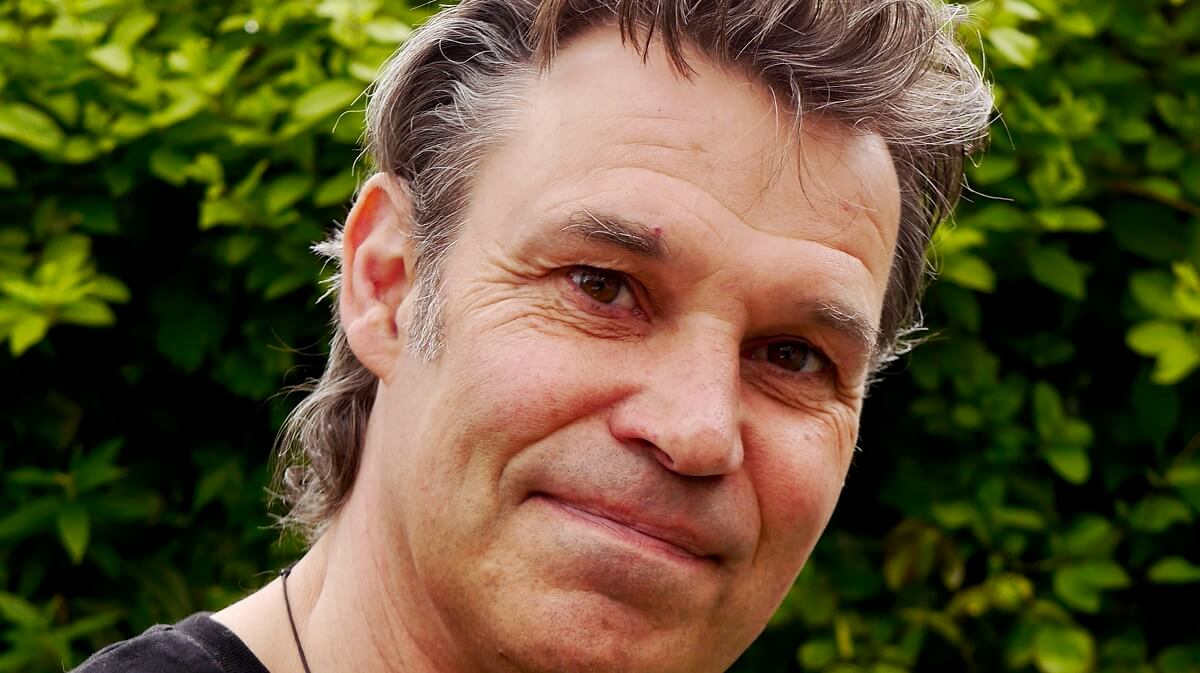 An image of Julian Hight looking straight at the camera, with leaves in the background