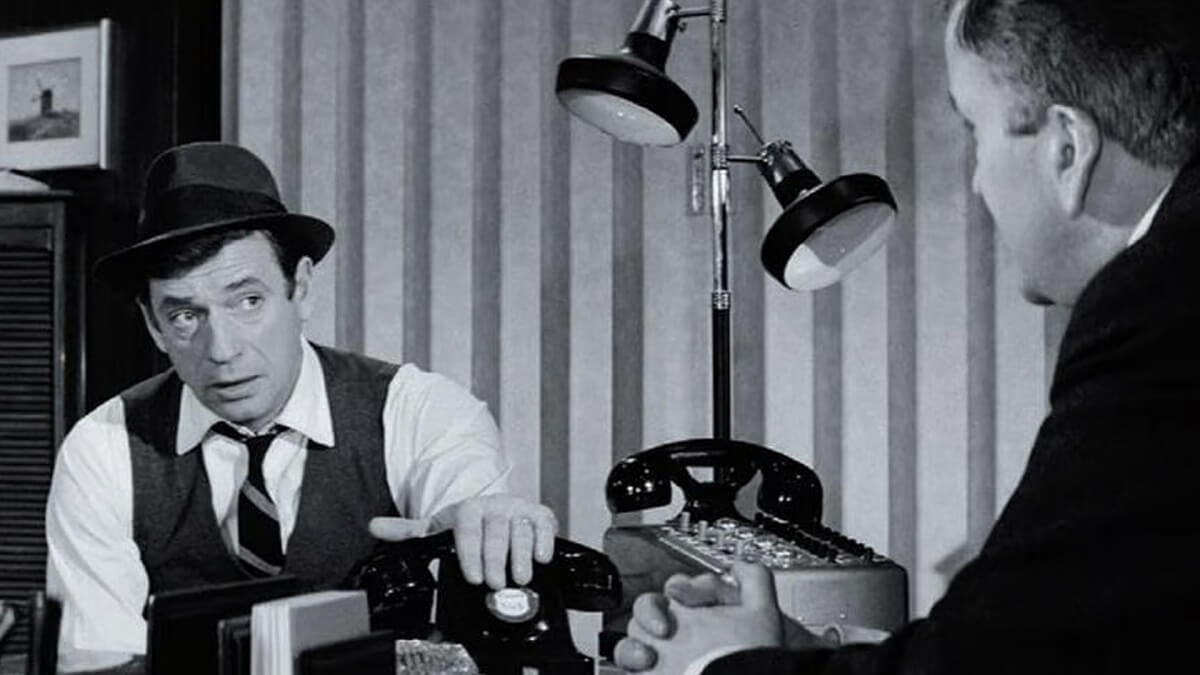 A still from the film showing two men seated near a lamp and telephones
