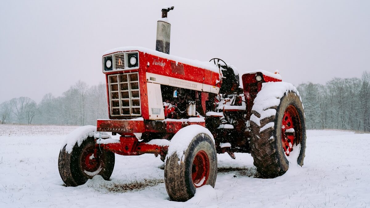 A red tractor in a snow-covered field, with trees is the background