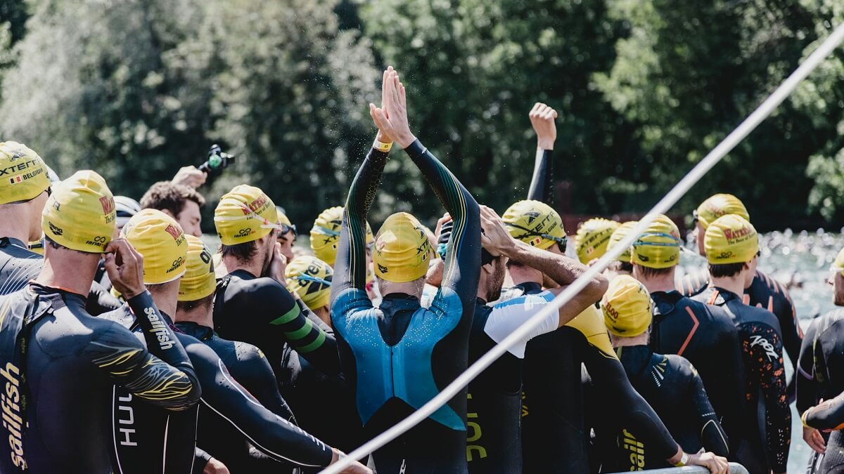 A group of competitors, wearing wet suits and swimming caps, waiting to start a triathlon