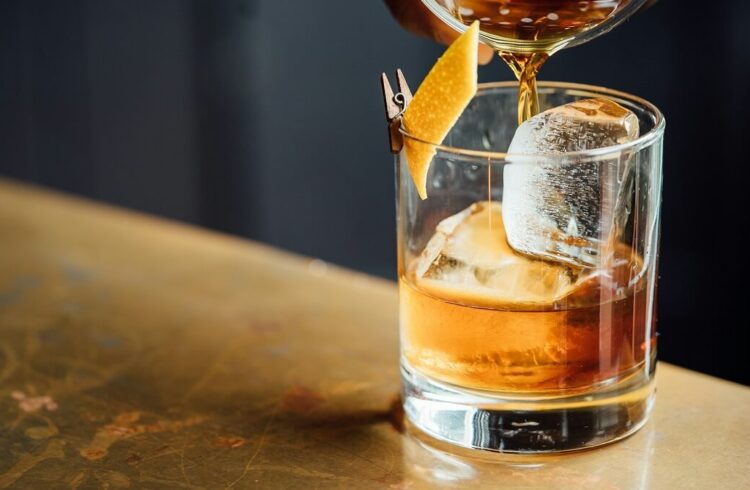 A glass on a table containing a drink with ice