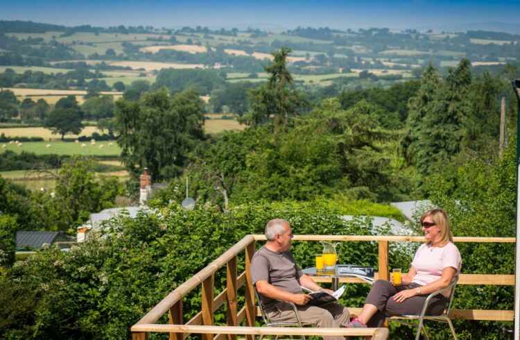 Two guests seated on chairs on the decking, enjoying the views over the countryside