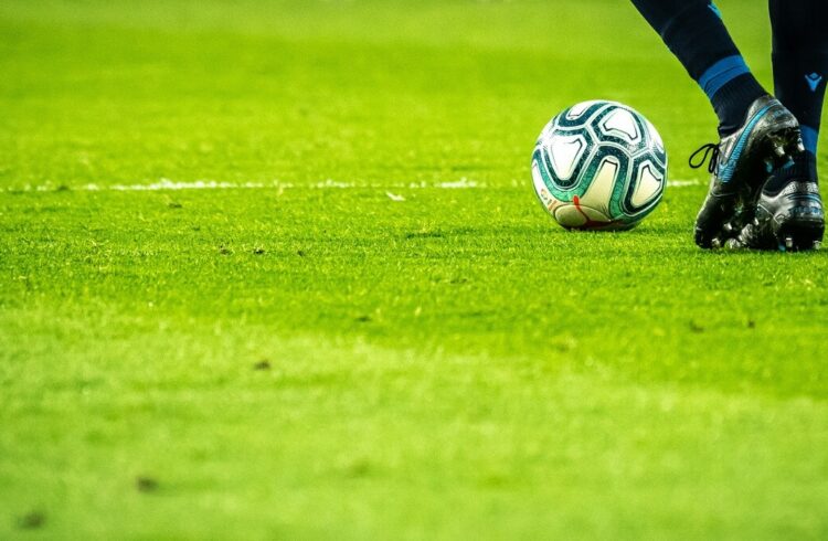 A football player's lower legs, boots and a football on a pitch