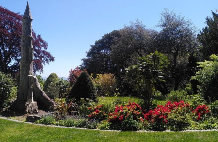 The garden at The Dell House with shrubs, flowers, trees and a sculpture