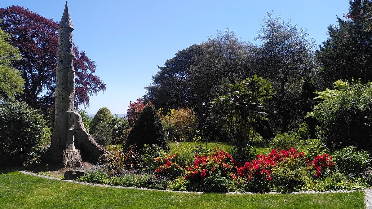 The garden at The Dell House with shrubs, flowers, trees and a sculpture